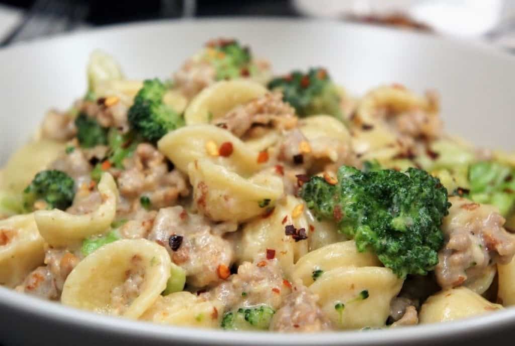 Orecchiette with Italian Sausage and Broccoli served in a white bowl and garnished with crushed red pepper flakes