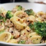 Orecchiette with Italian Sausage and Broccoli served in a white bowl and garnished with crushed red pepper flakes