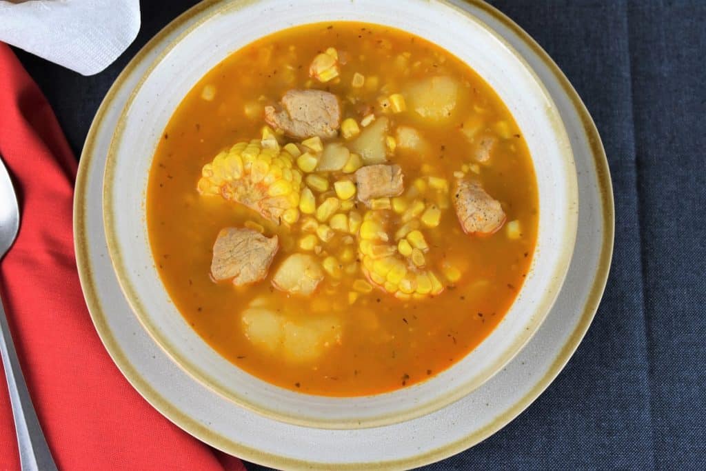 A close up Cuban Corn Stew, or guiso de maiz in Spanish is served in a light colored bowl loaded with corn, pork chunks, potatoes.
