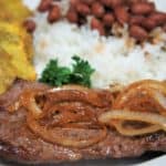 Cuban Cube Steak, topped with cooked onions and served with white rice, red beans and fried green plantains on the side.