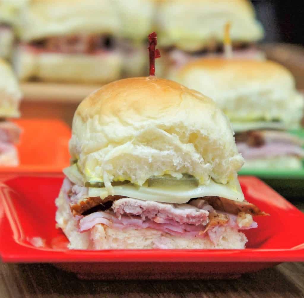 A close up of a cuban slider on a small red plate with other sliders in the background.
