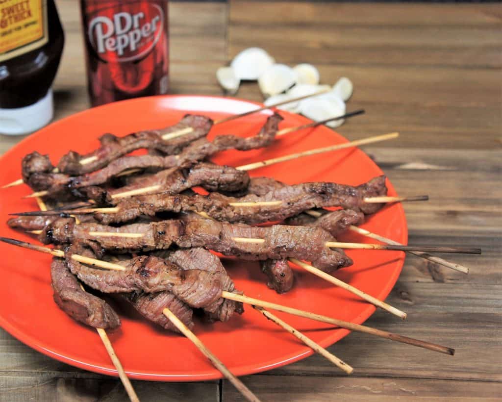 Dr Pepper marinated steak skewers arranged on an orange plate.