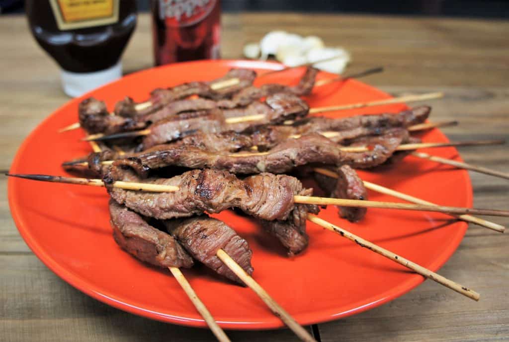 Dr Pepper marinated steak skewers arranged on an orange plate.