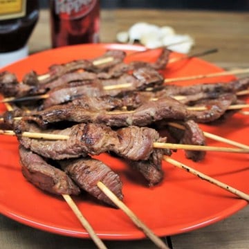 Dr Pepper marinated steak skewers arranged on an orange plate.