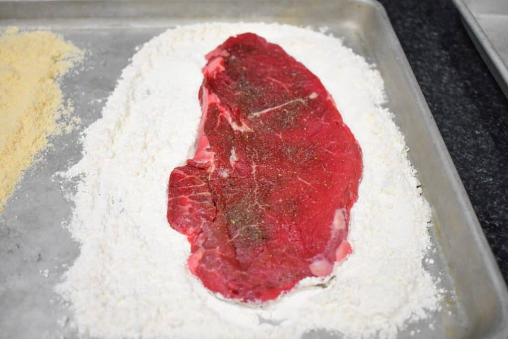 A large palomilla steak on a baking sheet covered with flour.