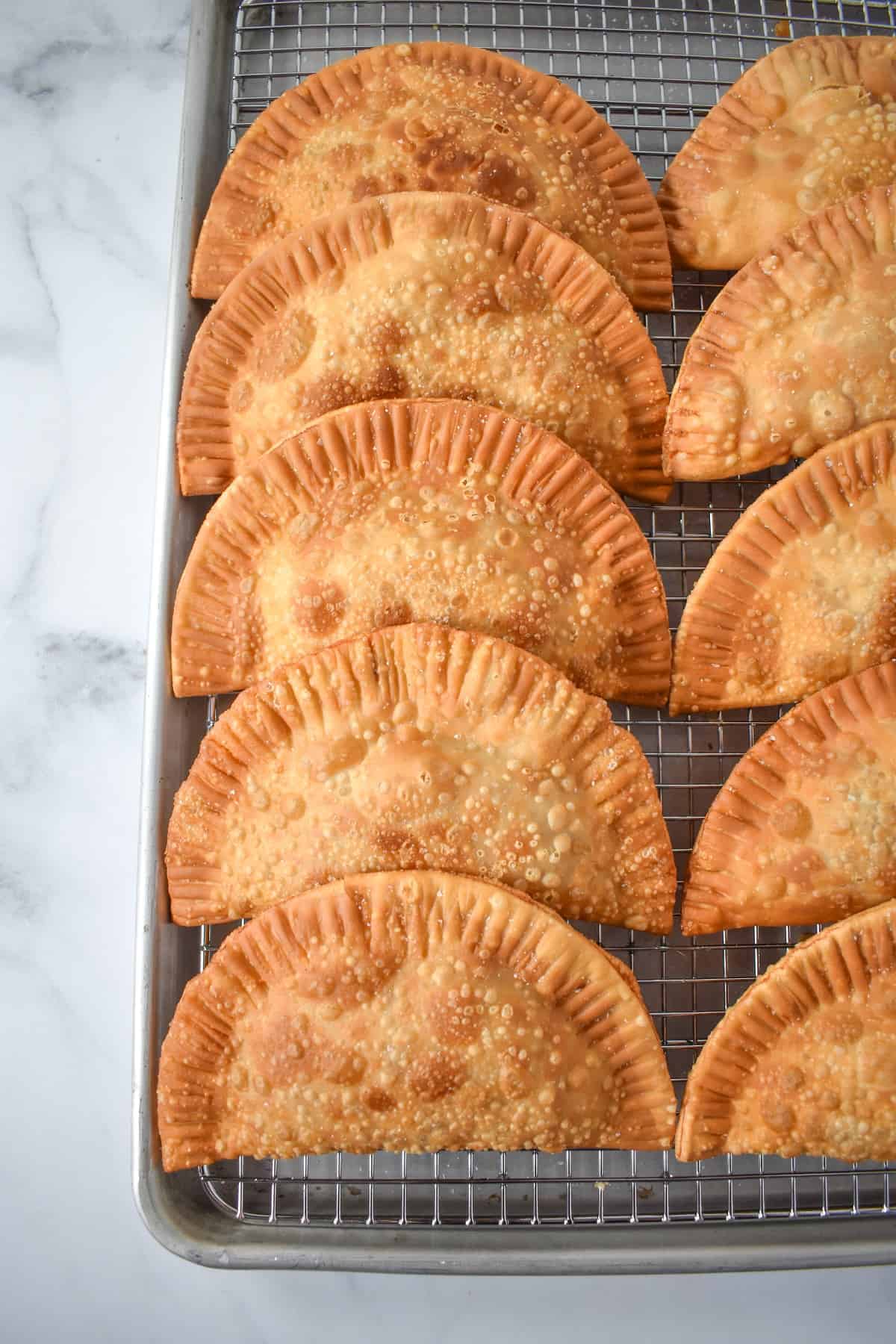 The fried empanadas set on a baking sheet lined with a cooling rack.