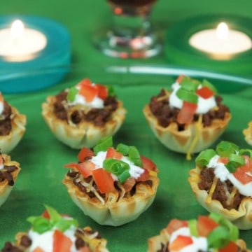 Fillo taco cups topped with sour cream, tomatoes and green onions arranged on a platter