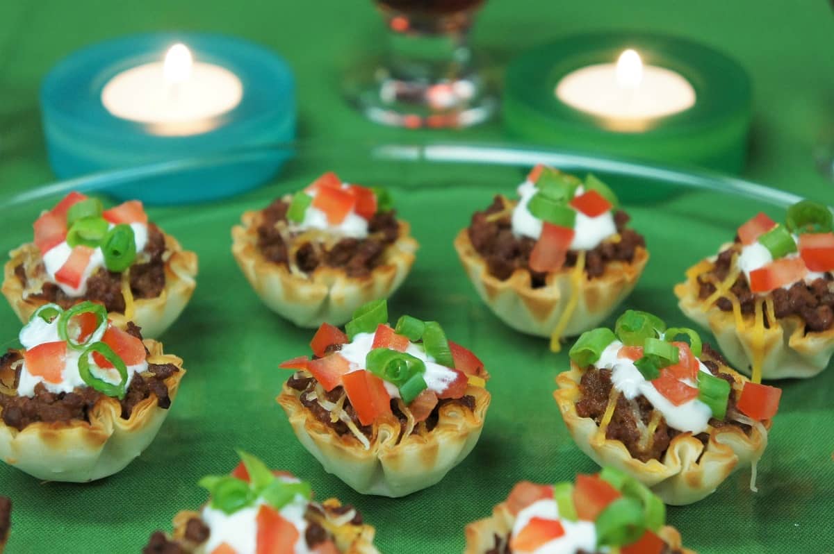 Fillo taco cups topped with sour cream, tomatoes and green onions arranged on a platter