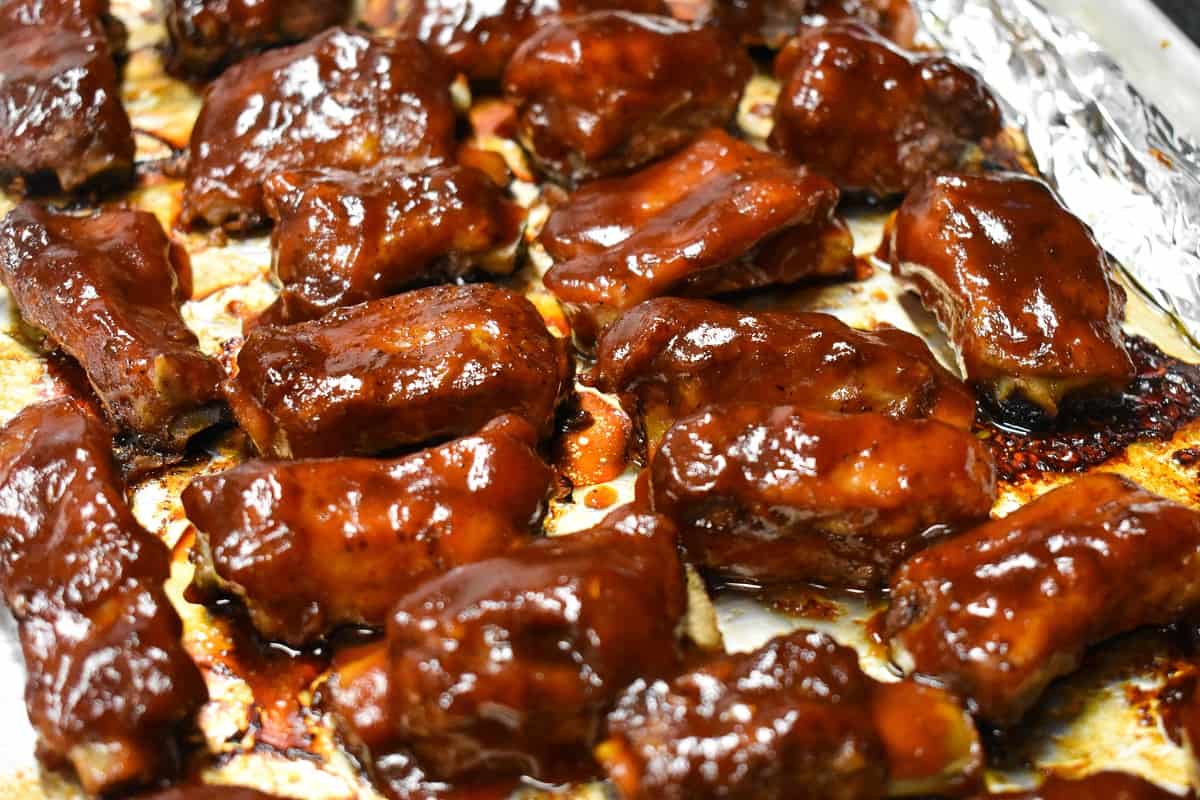 Barbecue riblets arranged on an aluminum foil lined baking sheet.