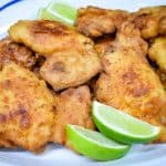 Fried chicken thighs arranged on a large white platter and served with lime wedges.