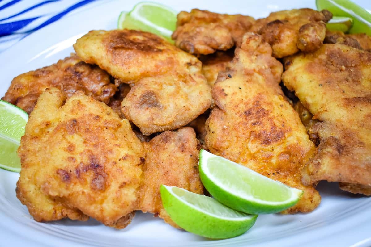Fried chicken thighs arranged on a large white platter and served with lime wedges.