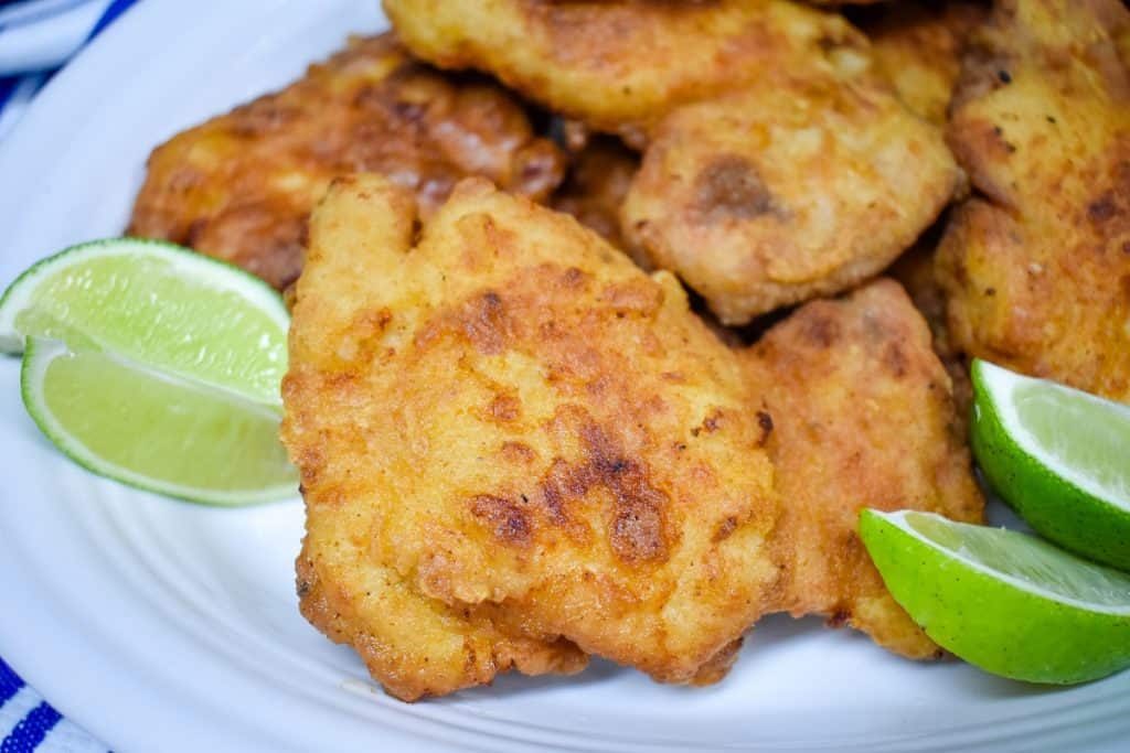 Fried chicken thighs arranged on a large white platter and garnished with lime wedges.