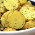 Gold potatoes, cut in half and tossed in a minced garlic and dill oil, served in a white rimmed blue bowl.