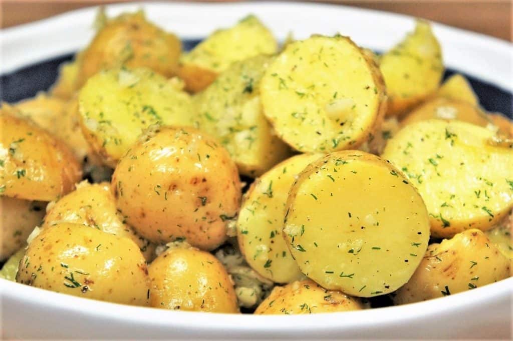 Gold potatoes, cut in half and tossed in a minced garlic and dill oil, served in a white rimmed blue bowl.