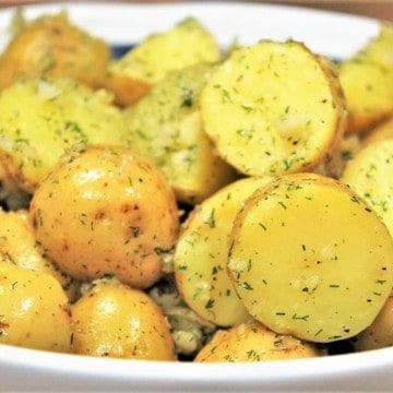 Gold potatoes, cut in half and tossed in a minced garlic and dill oil, served in a white rimmed blue bowl.