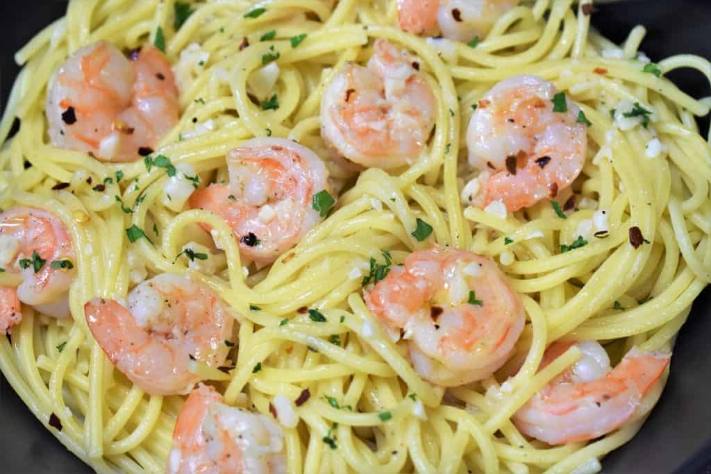 A close up picture of spaghetti topped with shrimp in a garlic oil and garnished with parsley.