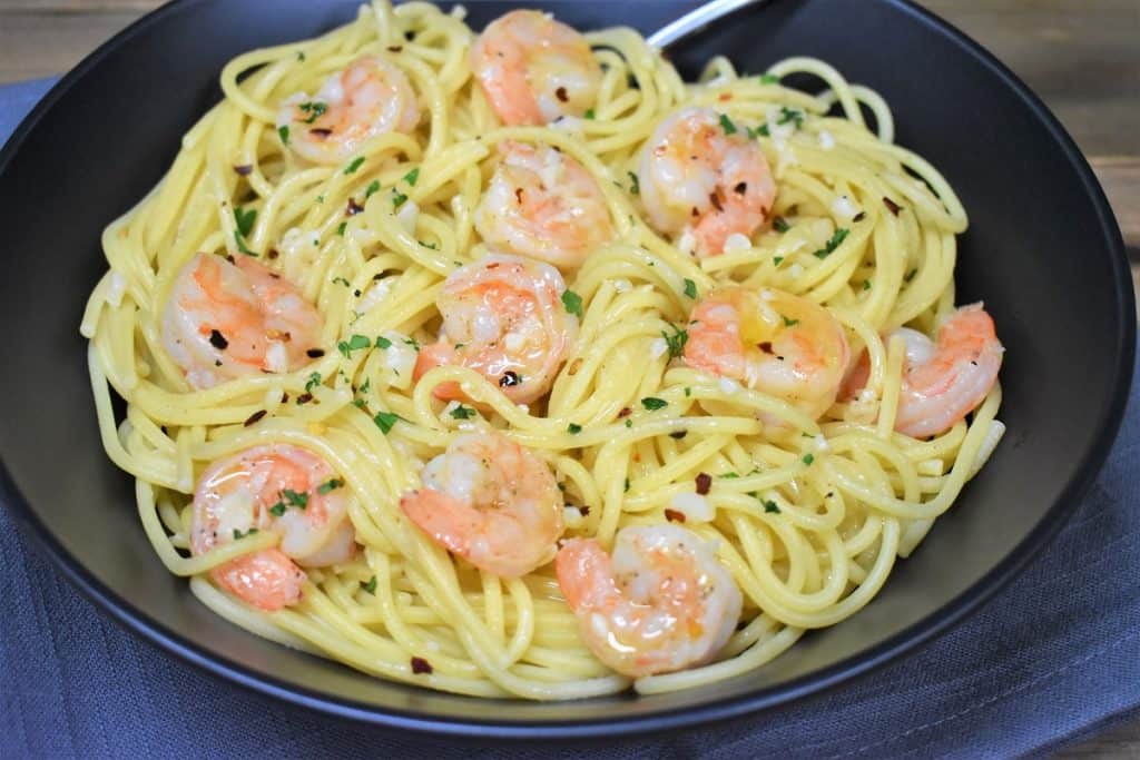 Spaghetti topped with shrimp in an oil and garlic sauce, garnished with parsley and served in a large black bowl.