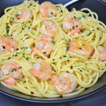 Spaghetti topped with shrimp in an oil and garlic sauce, garnished with parsley and served in a large black bowl.