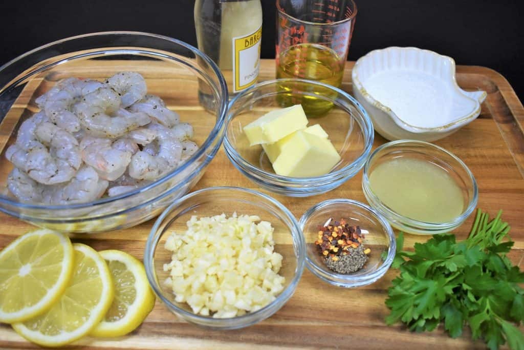 The ingredients for the garlic shrimp pasta recipe displayed on a wood cutting board.