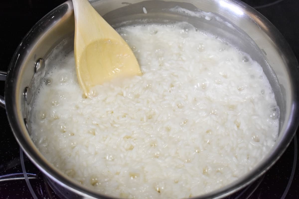 White rice in a saucepan where most of the water has cooked away with a wood spoon in the rice.