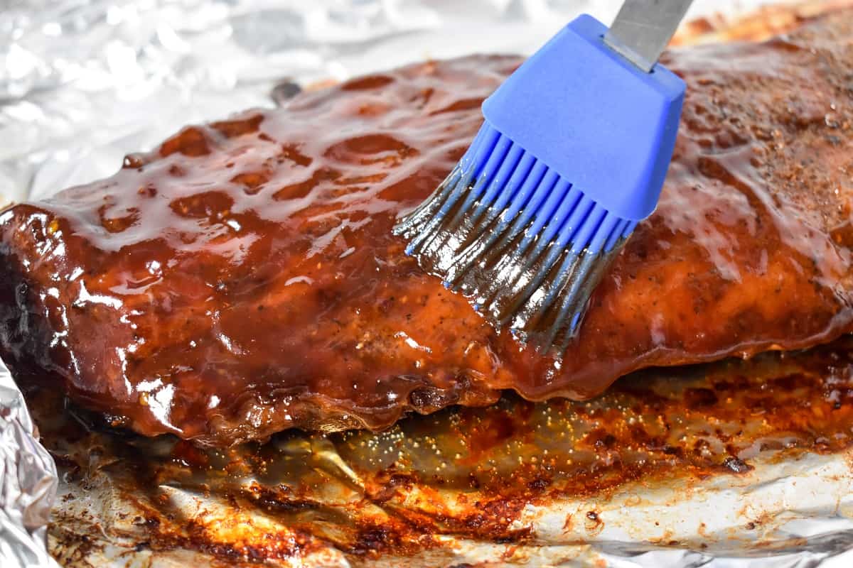 An image of the cooked ribs being brushed with the barbecue sauce with a blue brush.