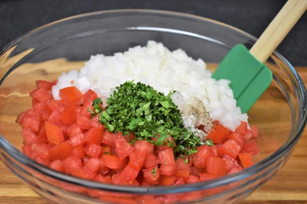 Diced tomatoes, onions, chopped cilantro, salt and pepper in a large, clear bowl.