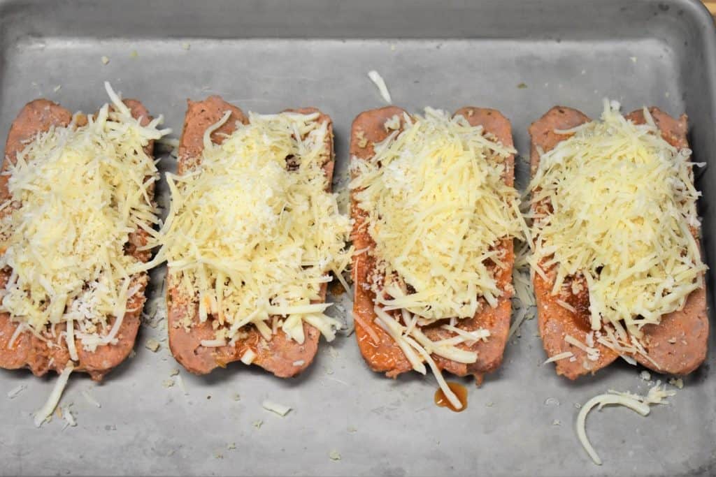 Italian Sausage Parmigiana unbaked on a metal baking topped with tomato sauce, cheese and breadcrumbs