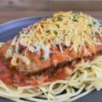Italian Sausage Parmigiana on a generous bed of spaghetti topped with red sauce served on a gray plate.