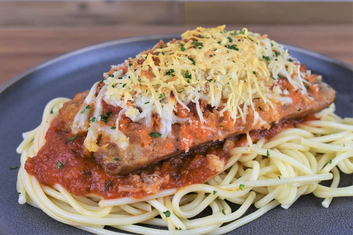 Italian Sausage Parmigiana on a generous bed of spaghetti topped with red sauce served on a gray plate.