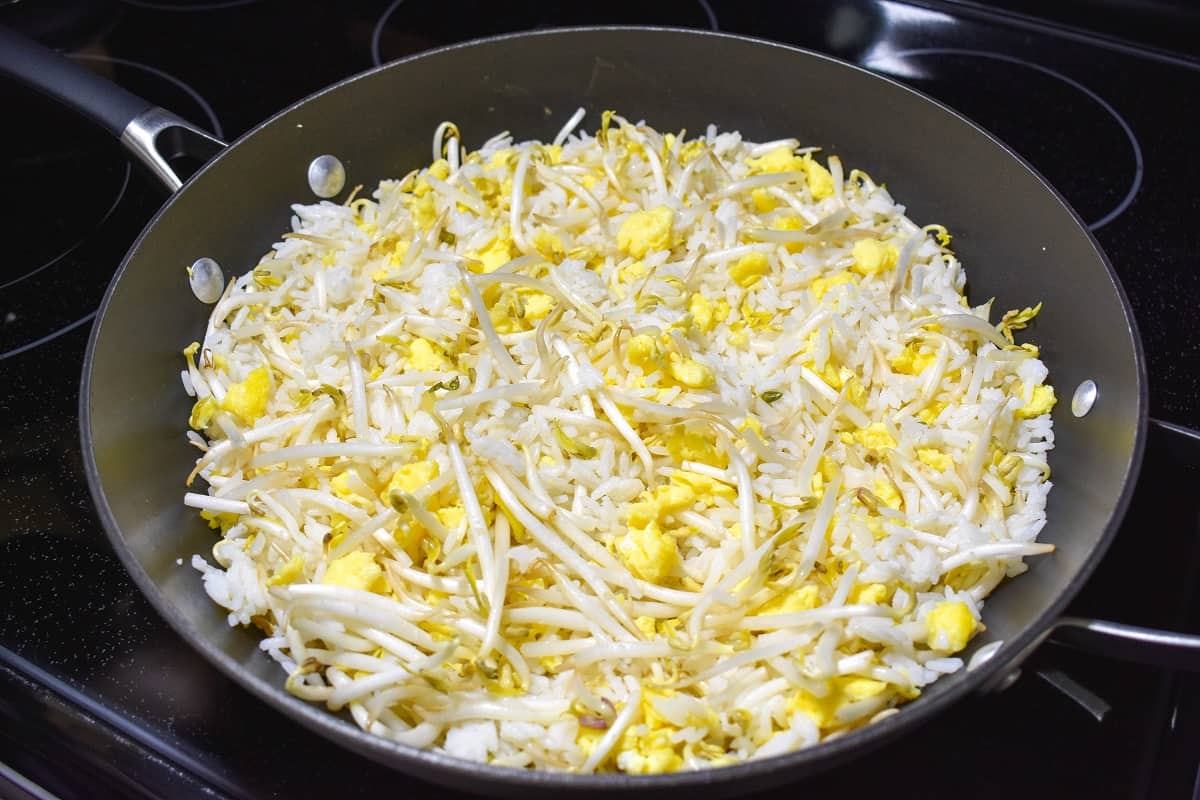 The white rice, scrambled egg and bean sprouts cooking in a large, black skillet.
