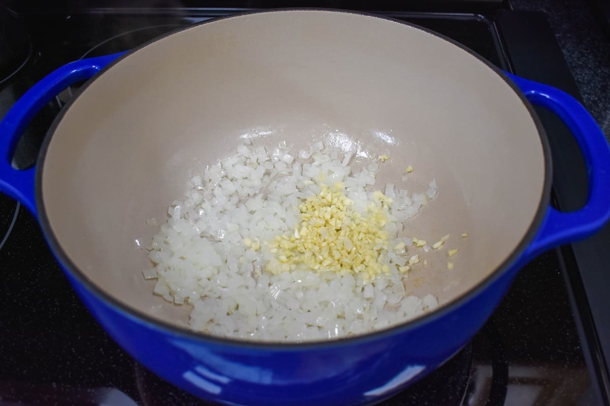 Onions and garlic cooking in a large, blue pot with an off-white inside.