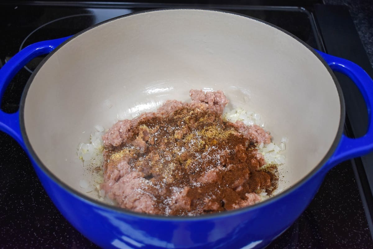 Ground turkey and a seasoning mix in a large blue pot with an off-white inside.