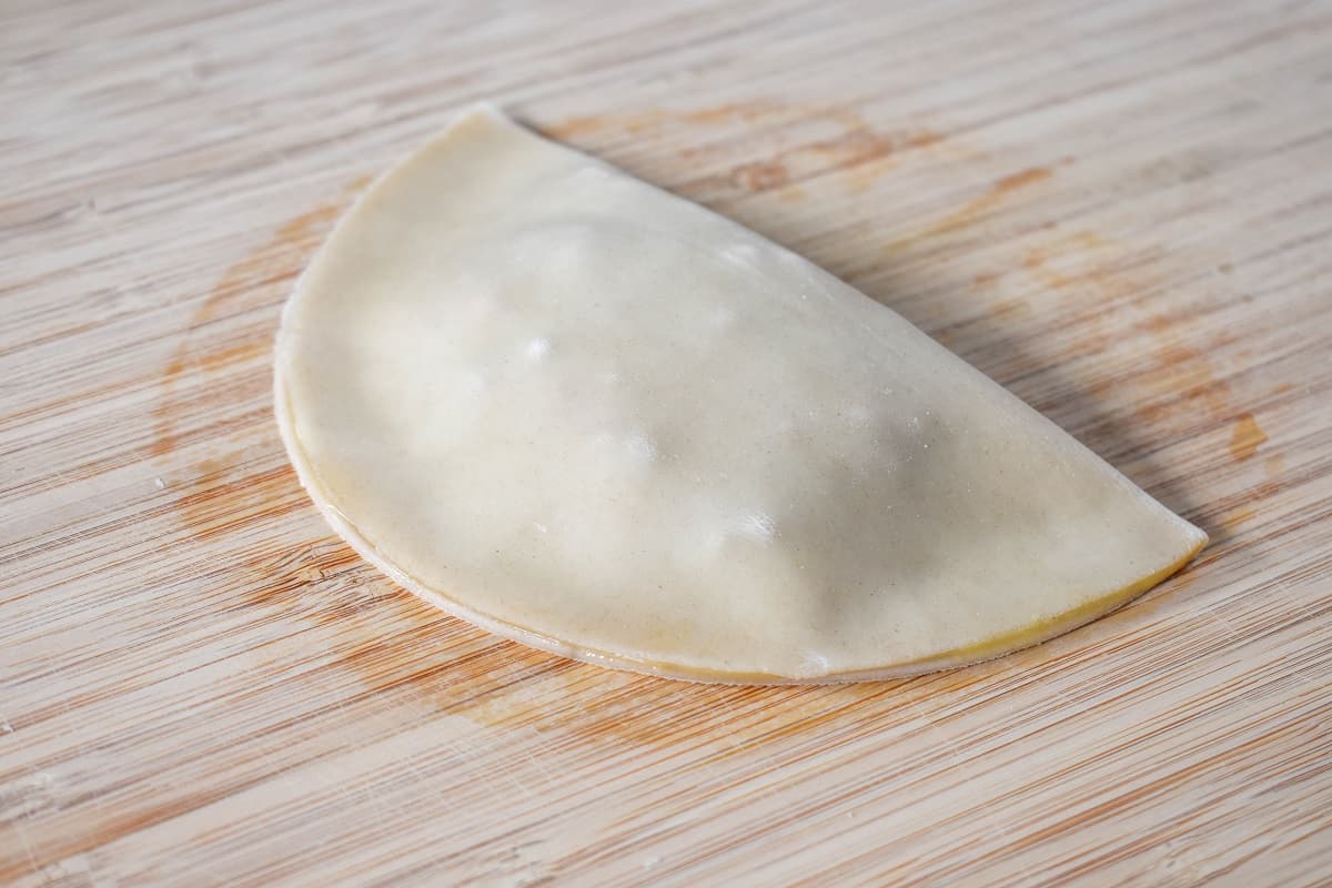 A filled dough disk folded in half to make a half moon set on a wood cutting board.