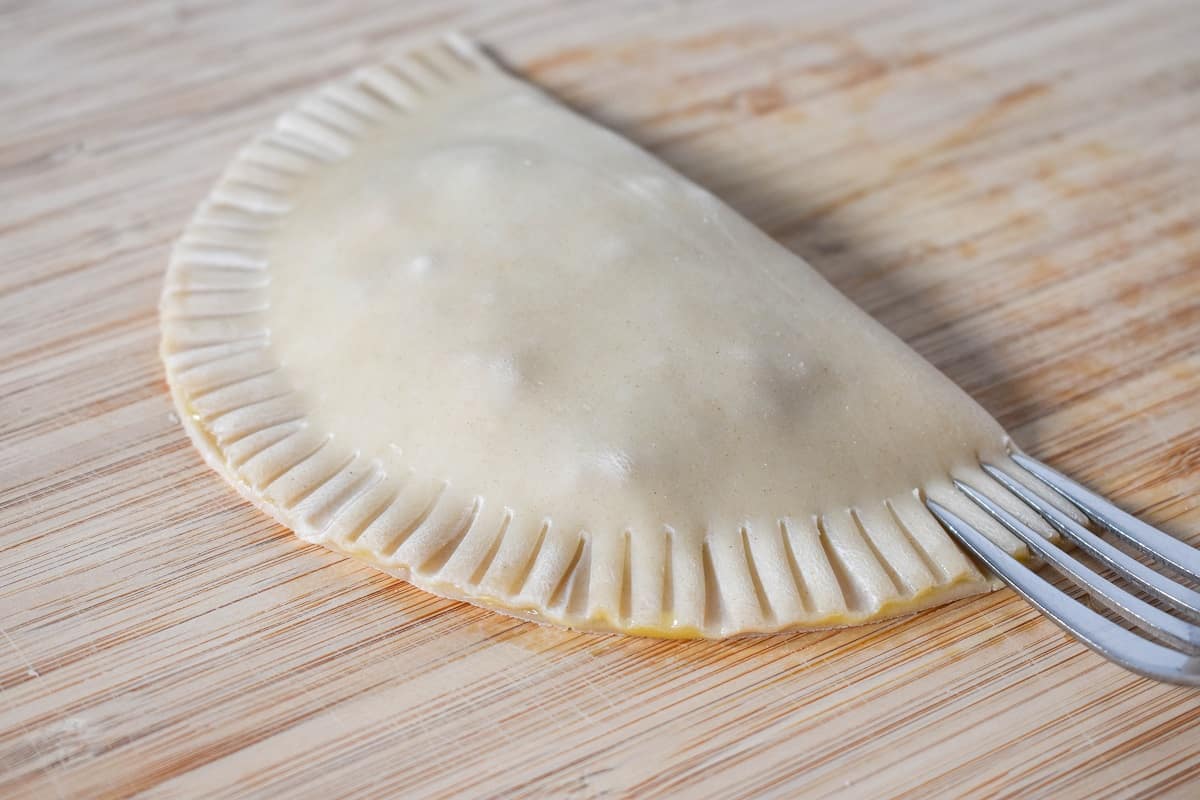 An empanada with the edges crimped by a fork, set on a wood cutting board.