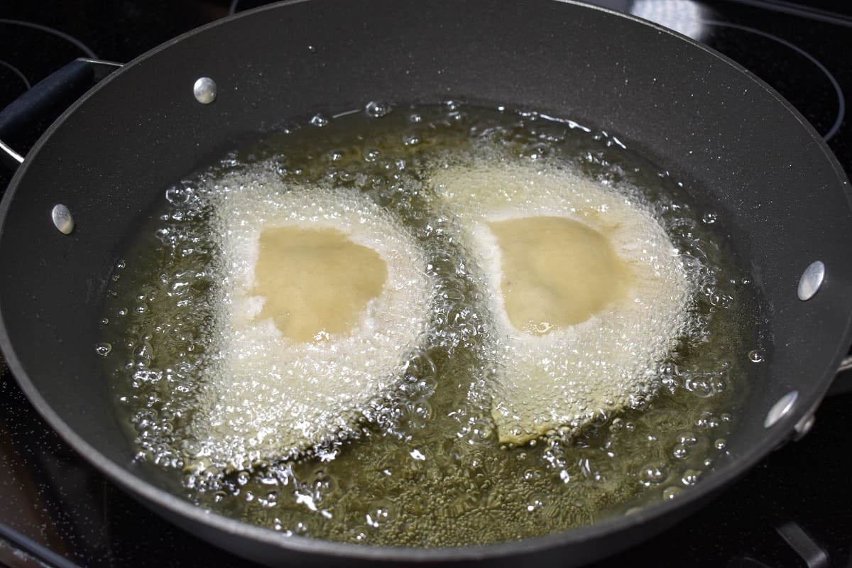 Two empanadas frying in a large, black skillet.