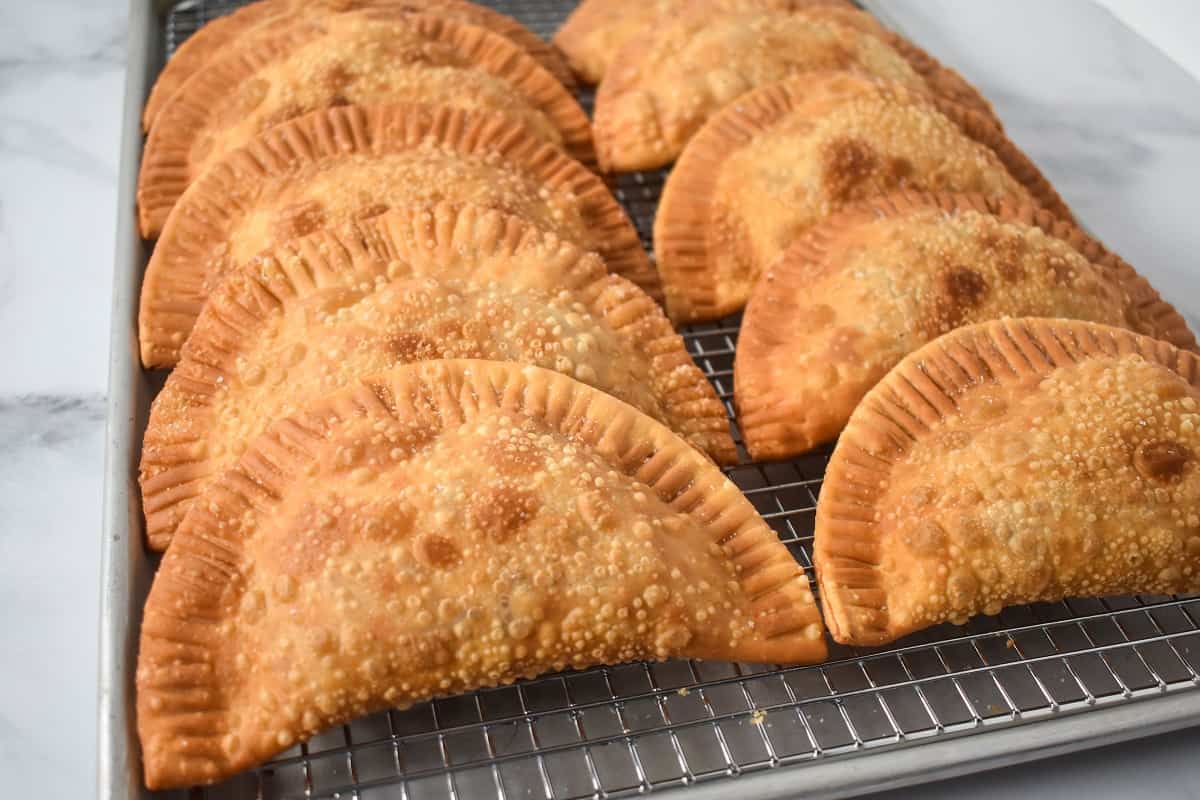 An image of ten fried empanadas arranged on a baking sheet lined with a cooling rack.