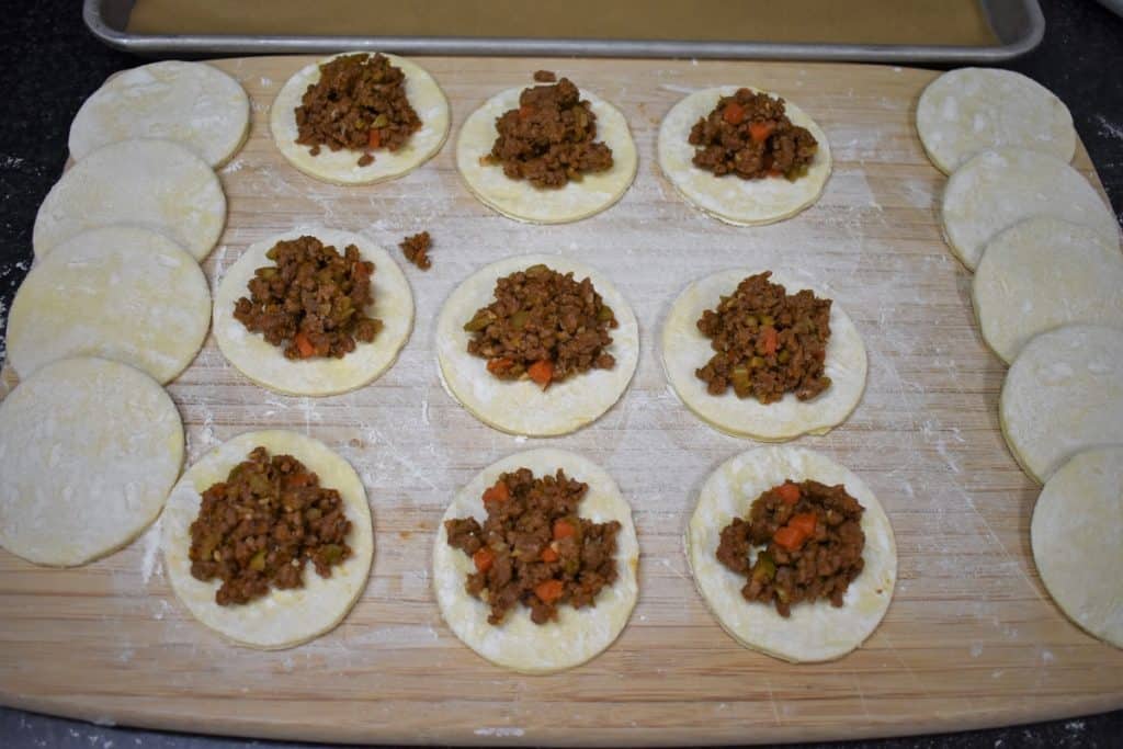 Nine puff pastry rounds topped with ground beef on a lightly floured cutting board