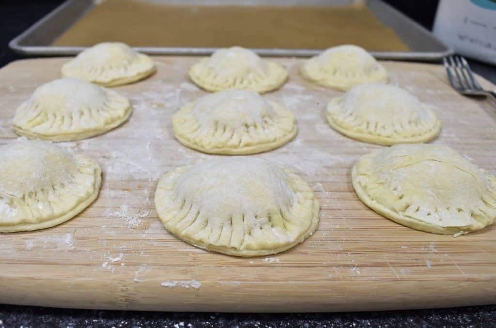 Nine unbaked Pastelitos de Carne on a lightly floured cutting board