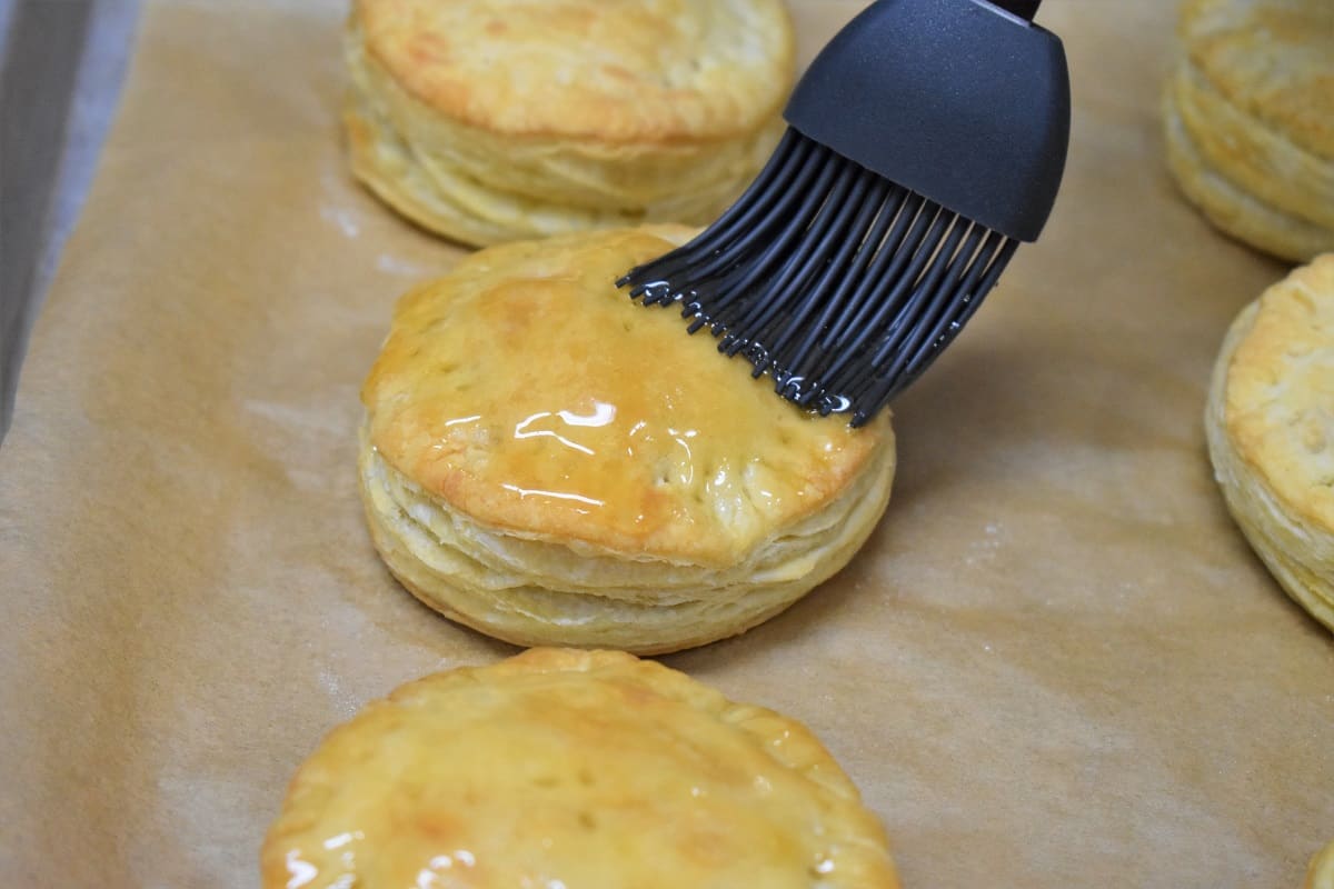 Pastelito de carne being glazed with honey with a gray pastry brush