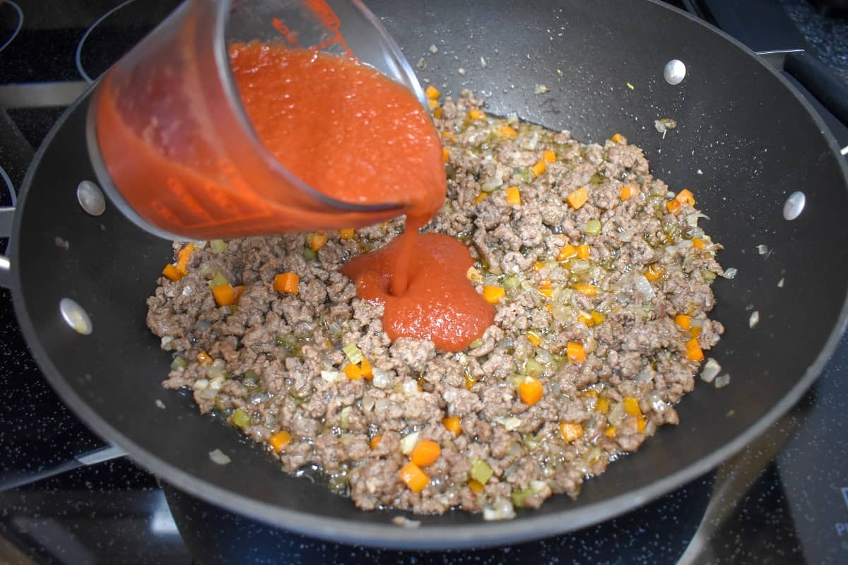 An image of tomato sauce being added to browned ground beef.