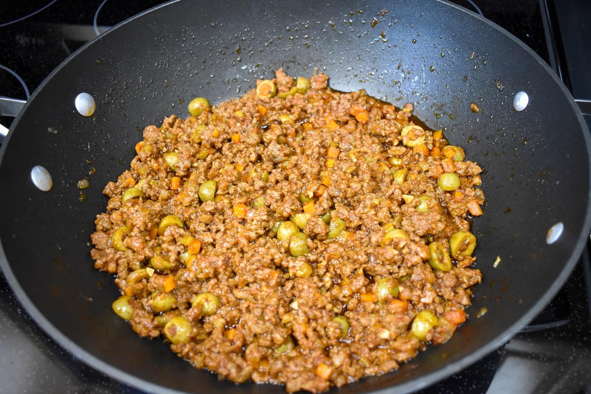 An image of cooked picadillo in a large, black skillet.
