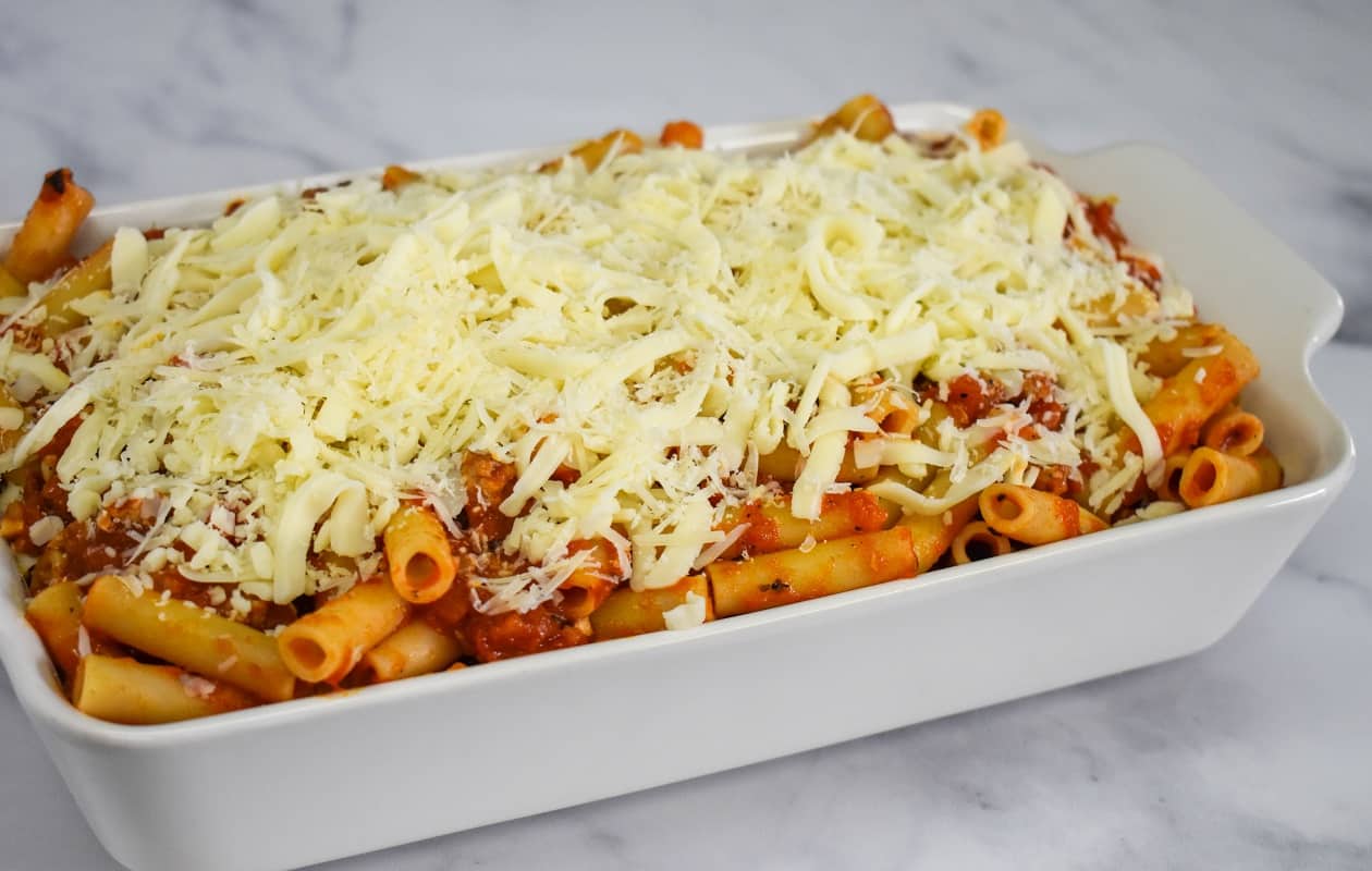 The prepared ziti, sauce and cheese in a white casserole dish, before baking.