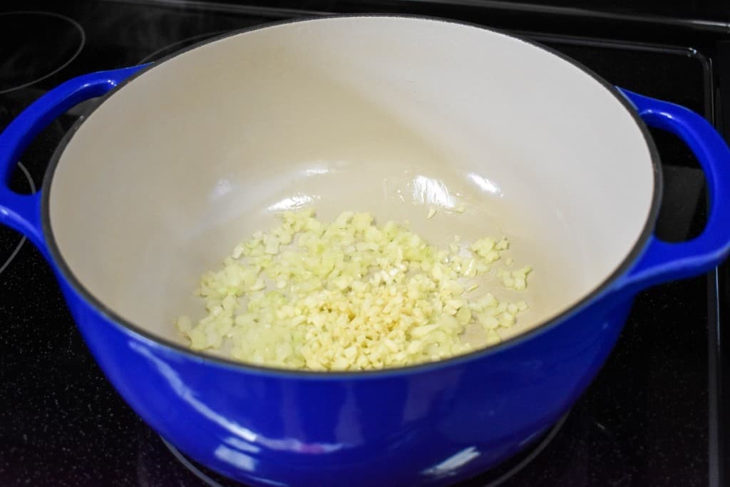 Diced onions and garlic cooking in a large blue pot.