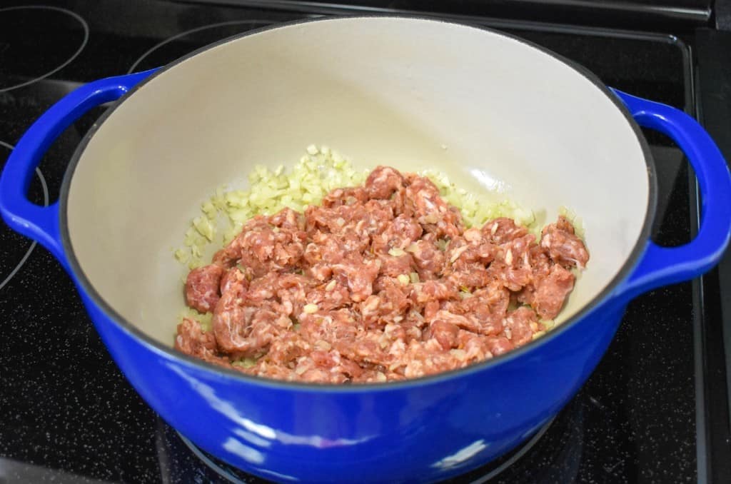 Sausage cooking with the onions and garlic in a large blue pot.