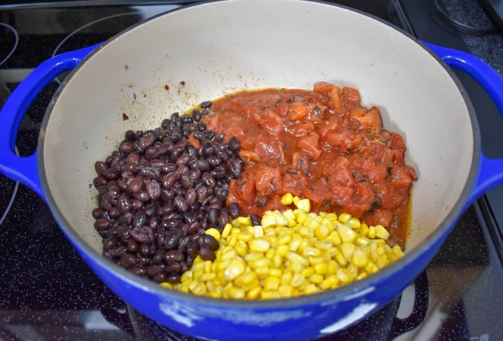 Black beans, diced tomatoes and corn in a large blue pot with a white inside.