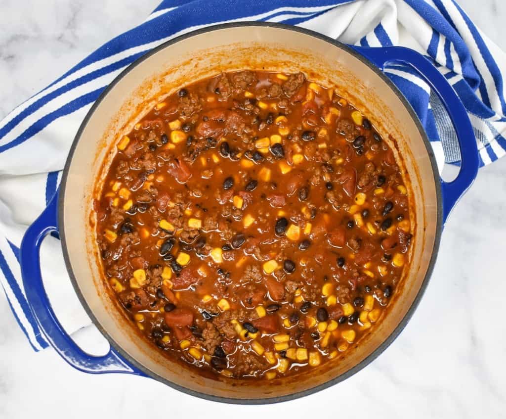 An overhead image of the sauce that's been cooked, it's still in the blue pot with a blue and white striped kitchen towel on a white table.