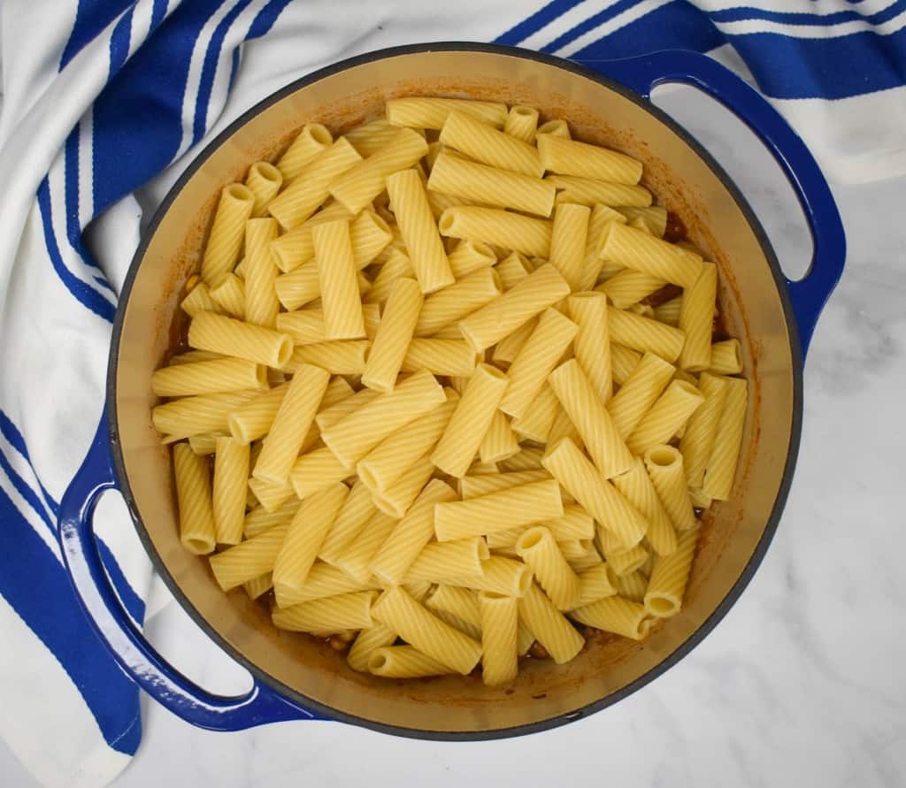 An overhead image of the pasta set on top of the sauce, it's still in the blue pot with a blue and white striped kitchen towel on a white table.