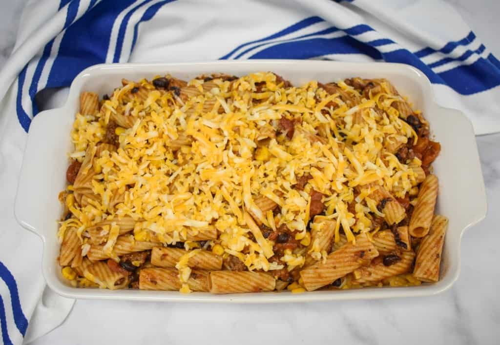 The built casserole, in a white dish, before baking. There is a blue and white kitchen towel behind it.