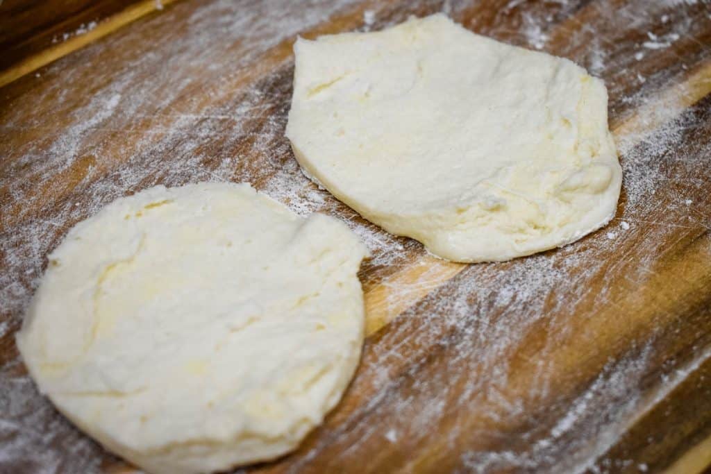 A raw biscuit, split in half on a floured wood cutting board.