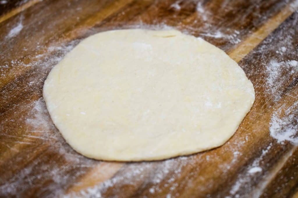 A rolled out biscuit on a floured wood cutting board.